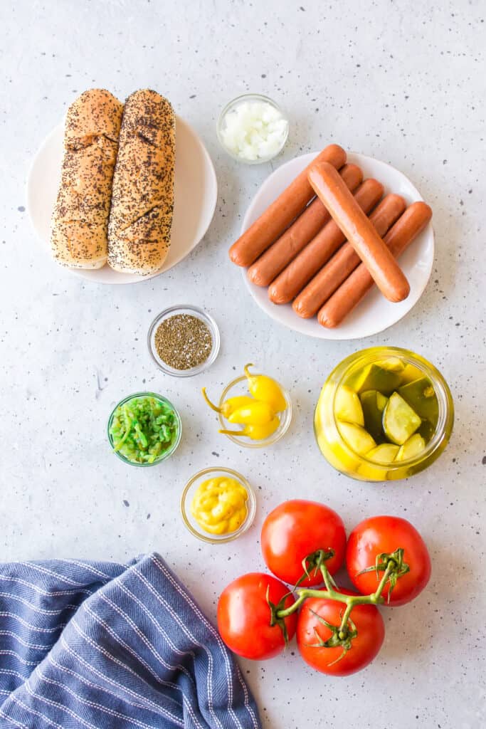 Ingredients for authentic Chicago Hot Dogs including all-beef hot dogs, poppy seed buns, sport peppers, relish, mustard, tomatoes, onions, pickles, and celery salt