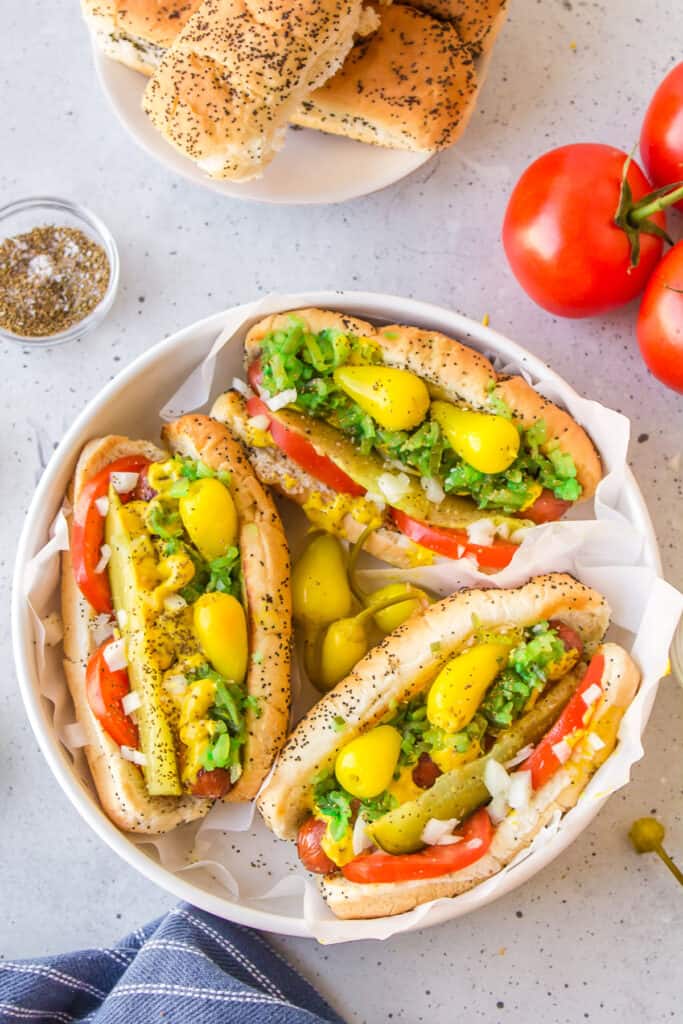 Three authentic Chicago Hot Dogs with sport peppers, relish, tomatoes, onions, mustard, pickles, and celery salt