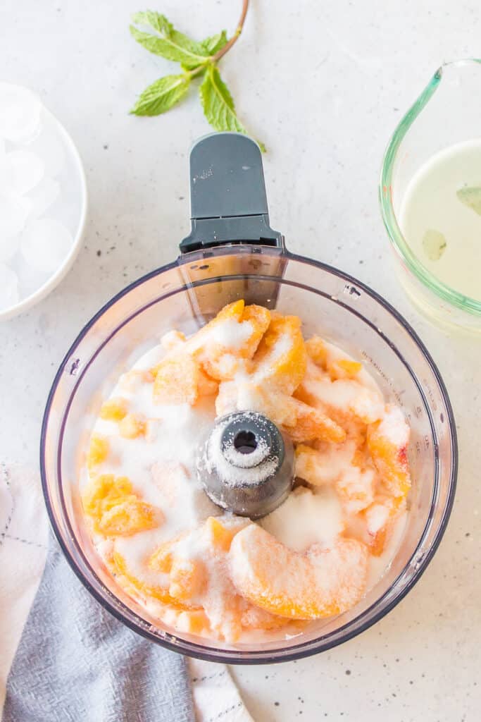 Frozen peaches and granulated sugar in a food processor before blending for a Frozen Peach Bellini.