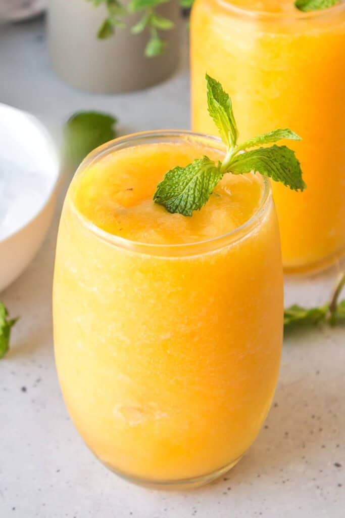 Creamy Frozen Peach Bellini garnished with fresh mint in a serving glass.