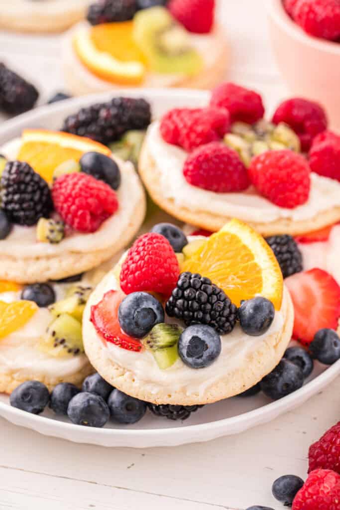 Platter of homemade Fruit Pizza Cookies topped with cream cheese frosting and fresh fruit.