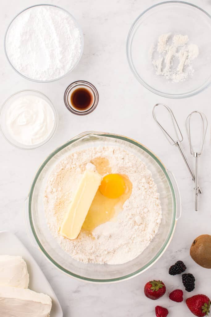 Sugar cookie mix, butter, egg, sour cream, and vanilla being added to a mixing bowl.