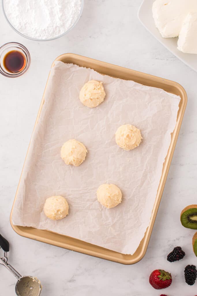 Scoops of Fruit Pizza Cookie dough portioned onto a parchment-lined baking sheet.