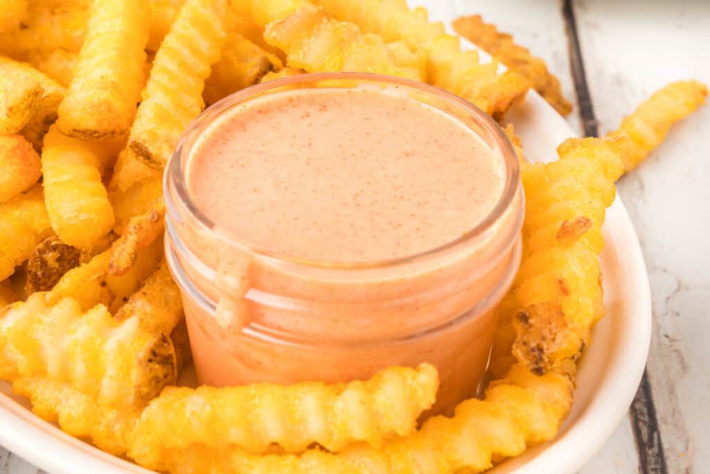 Close-up of creamy homemade Fry Sauce in a glass jar nestled among crinkle-cut French fries.