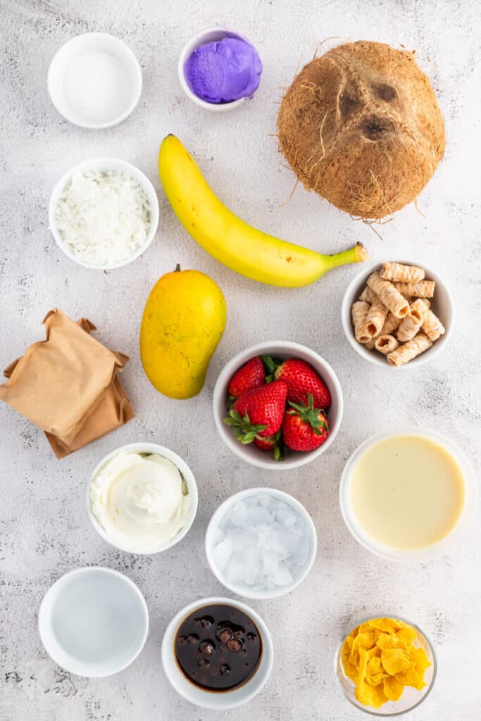 Ingredients for making homemade Halo Halo, including mango, strawberries, banana, ube ice cream, boba, coconut, sweetened condensed milk, and shaved ice.
