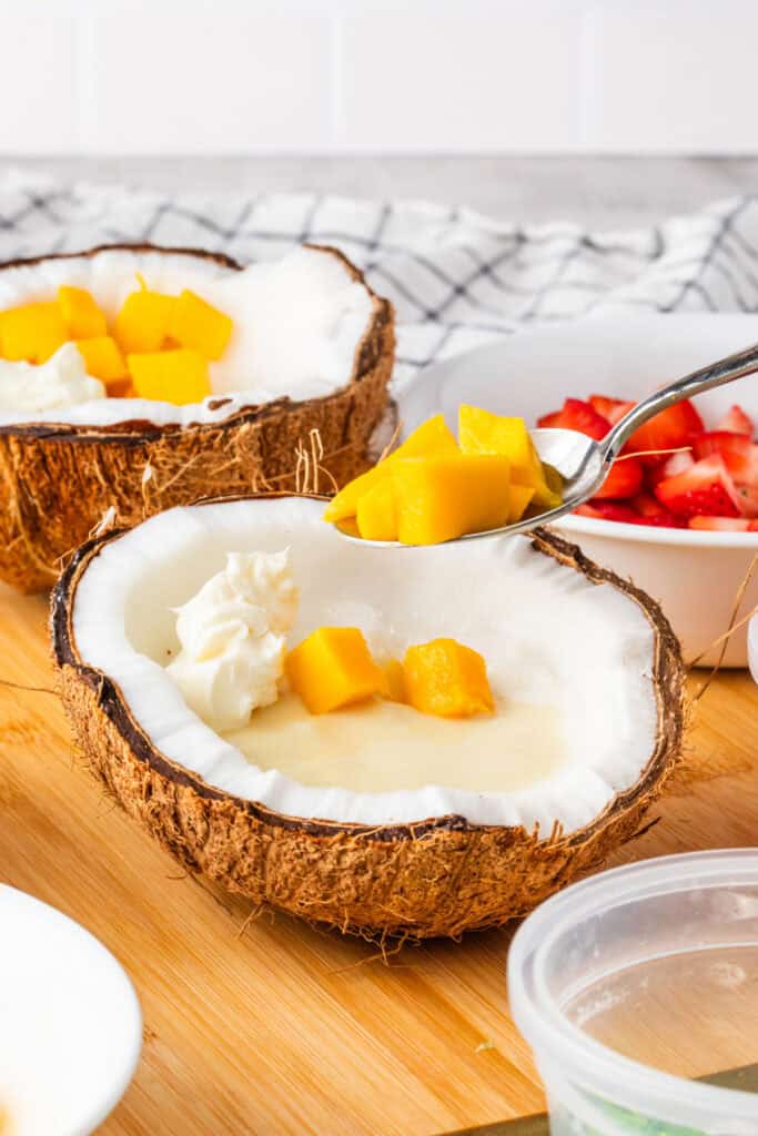 Diced mango arranged around the shaved ice in a coconut shell.