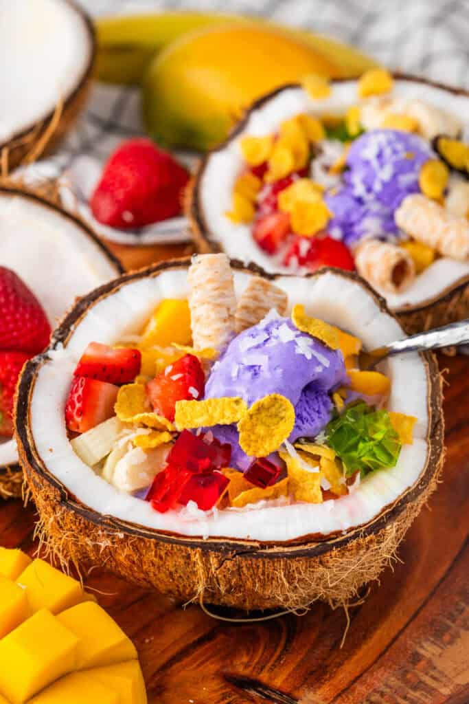 Halo Halo recipe served in a fresh coconut shell with ube ice cream, mango, strawberries, colorful gelatin, boba, and wafer cookies.