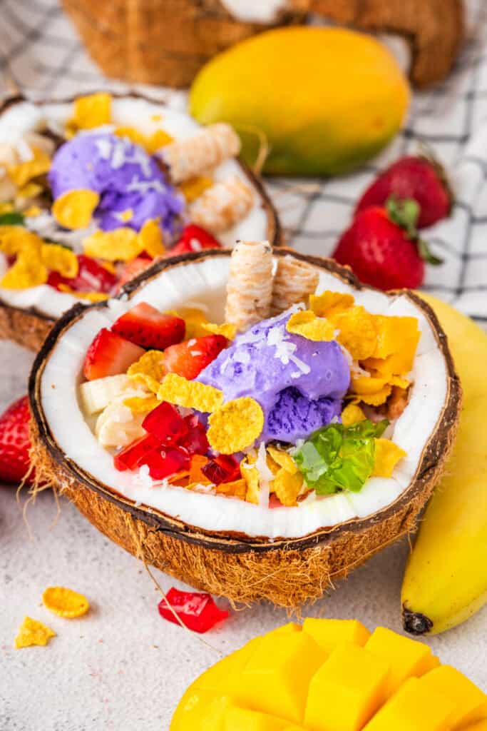 Filipino Halo Halo dessert topped with purple ube ice cream, fresh fruit, colorful gelatin, shredded coconut, and crispy corn flakes.