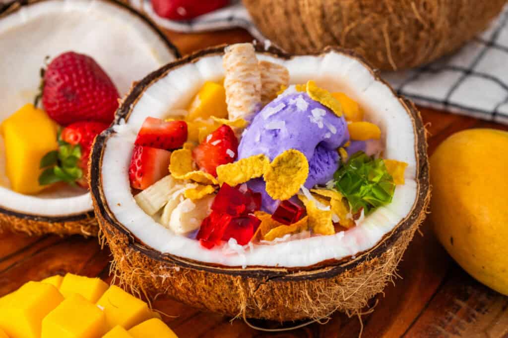 Close-up of homemade Halo Halo featuring ube ice cream, mango, strawberries, gelatin cubes, banana, corn flakes, and wafer cookies.