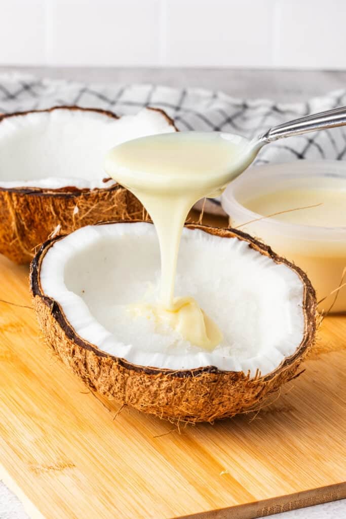 Drizzling sweetened condensed milk over shaved ice in a coconut shell.