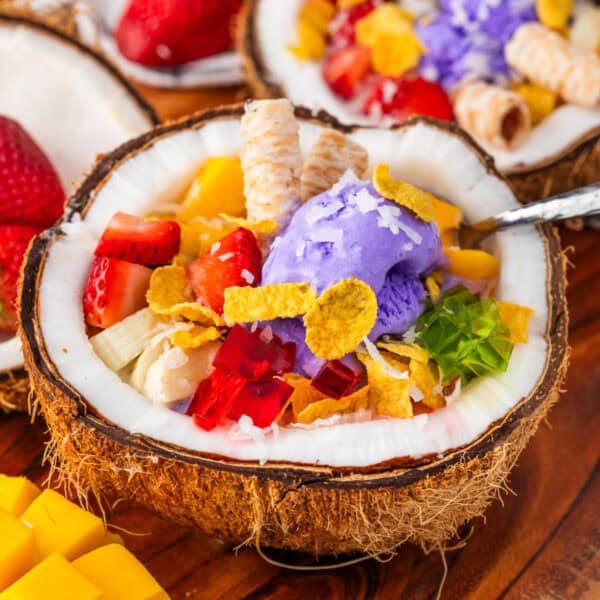 Homemade Halo Halo in a coconut shell topped with ube ice cream, fresh fruit, colorful gelatin, corn flakes, and wafer cookies.