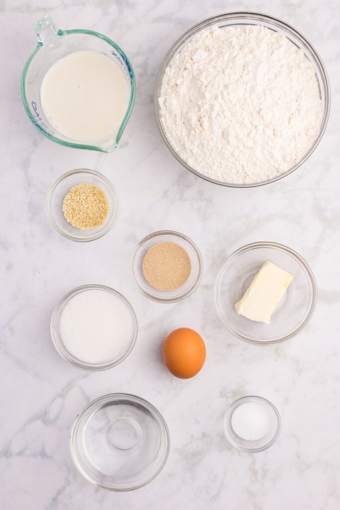 Ingredients needed to make homemade hamburger buns arranged on a marble countertop