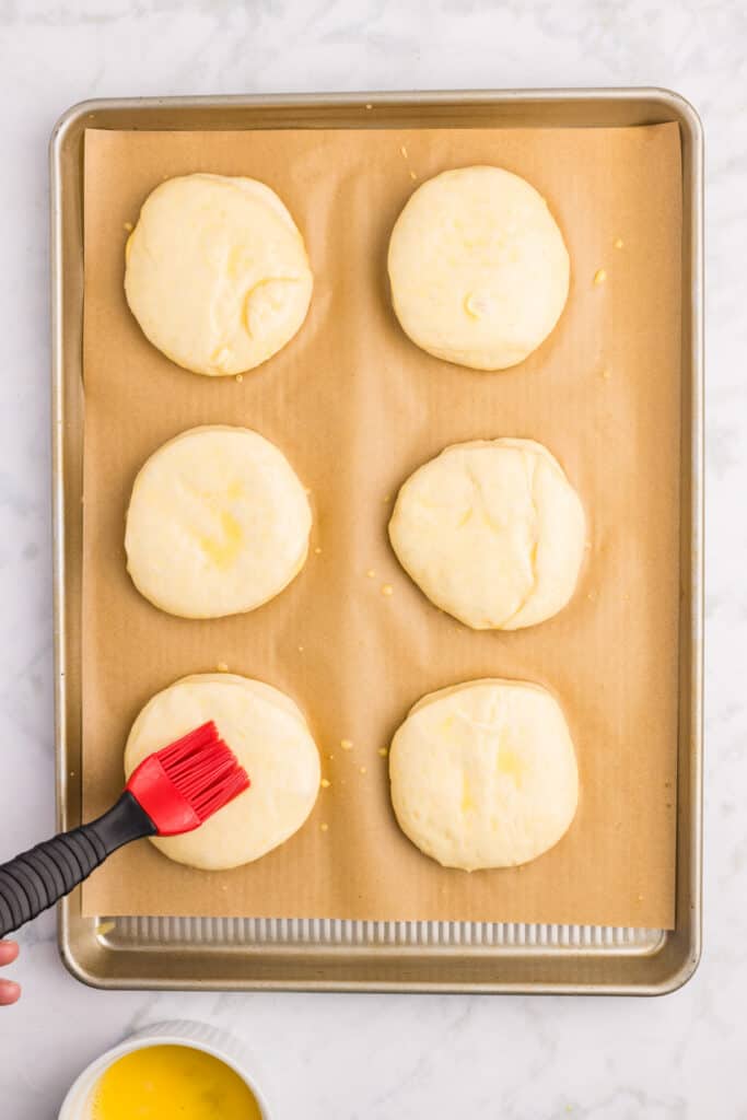 Brushing homemade hamburger buns with egg wash before baking