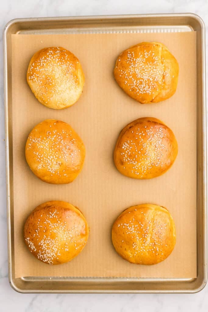 Freshly baked homemade hamburger buns with sesame seeds cooling on the baking sheet