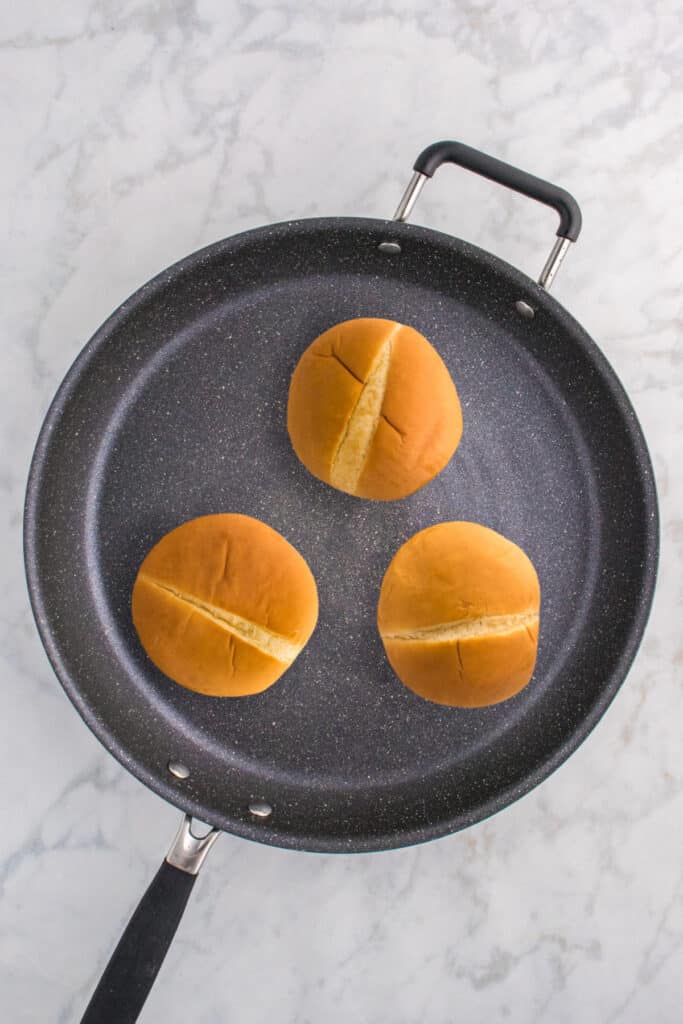 Buttered hamburger buns toasting in a skillet.