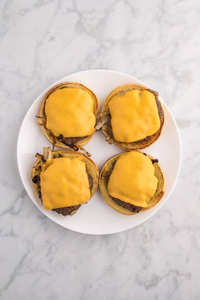 Cheeseburgers resting on toasted buns before adding toppings.