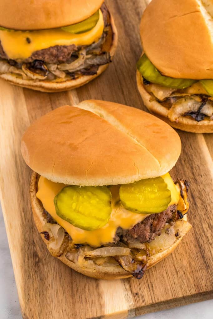 Oklahoma Onion Burger served on a wooden board with two burgers in the background.