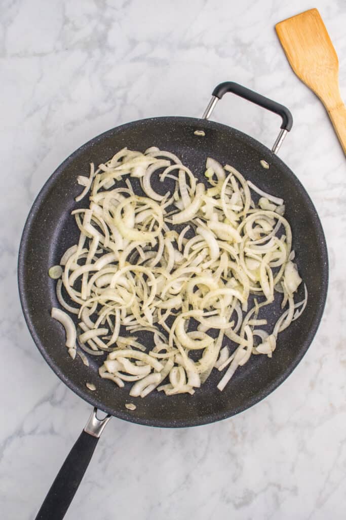 Sliced onions softening in a skillet before adding the burgers.
