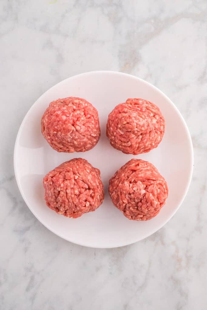 Four ground beef balls ready to be smashed into burgers.