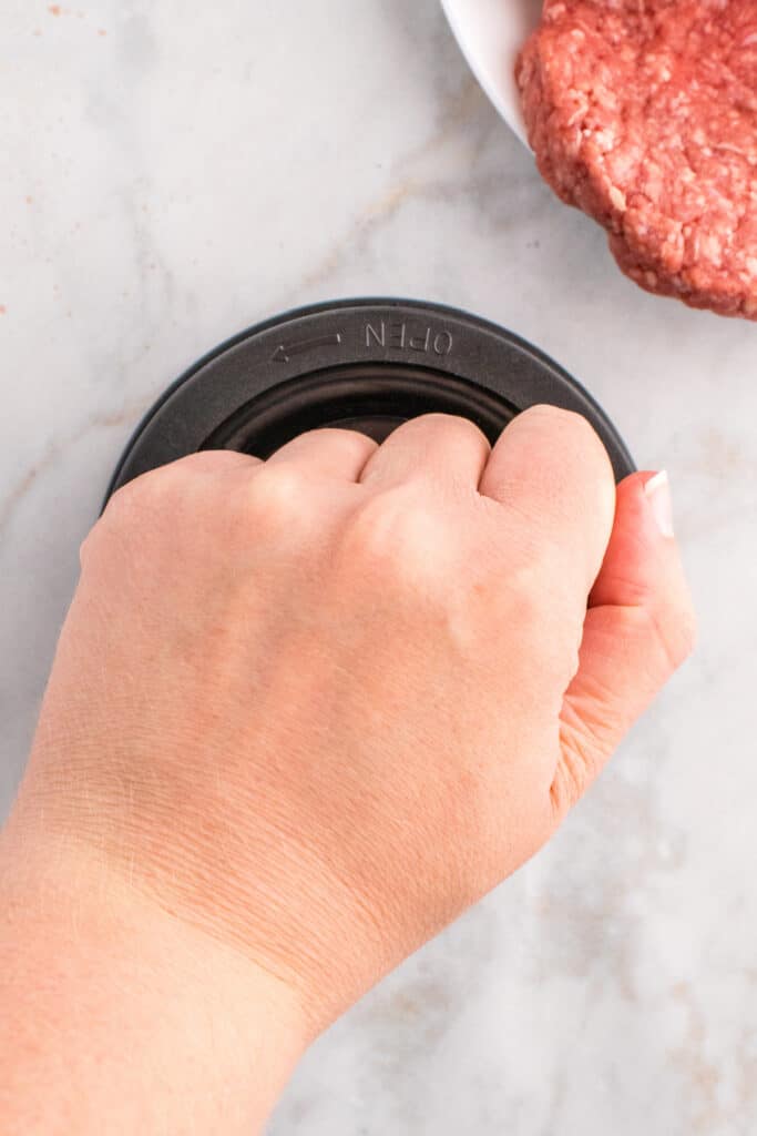 Pressing ground beef into a burger press with a hand.