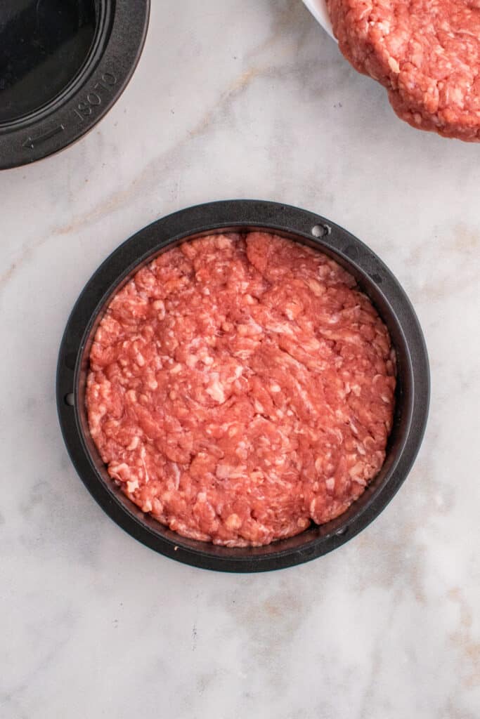 Flattened burger patty inside a burger press.