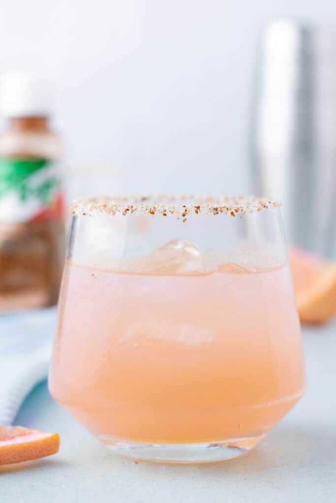 Paloma Cocktail with a Tajín-rimmed glass served over ice with fresh grapefruit.