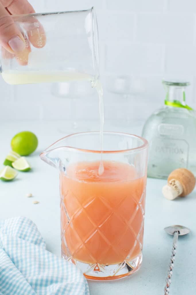 Pouring fresh lime juice into a mixing glass for a homemade Paloma Cocktail.