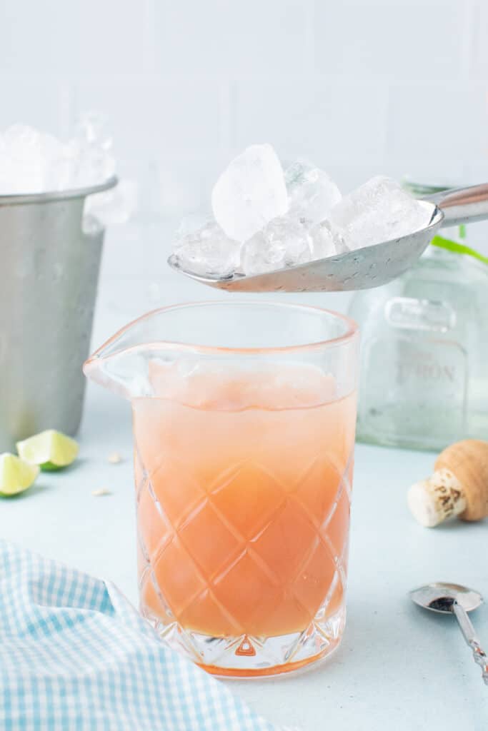 Adding ice to a mixing glass before stirring a fresh grapefruit cocktail.