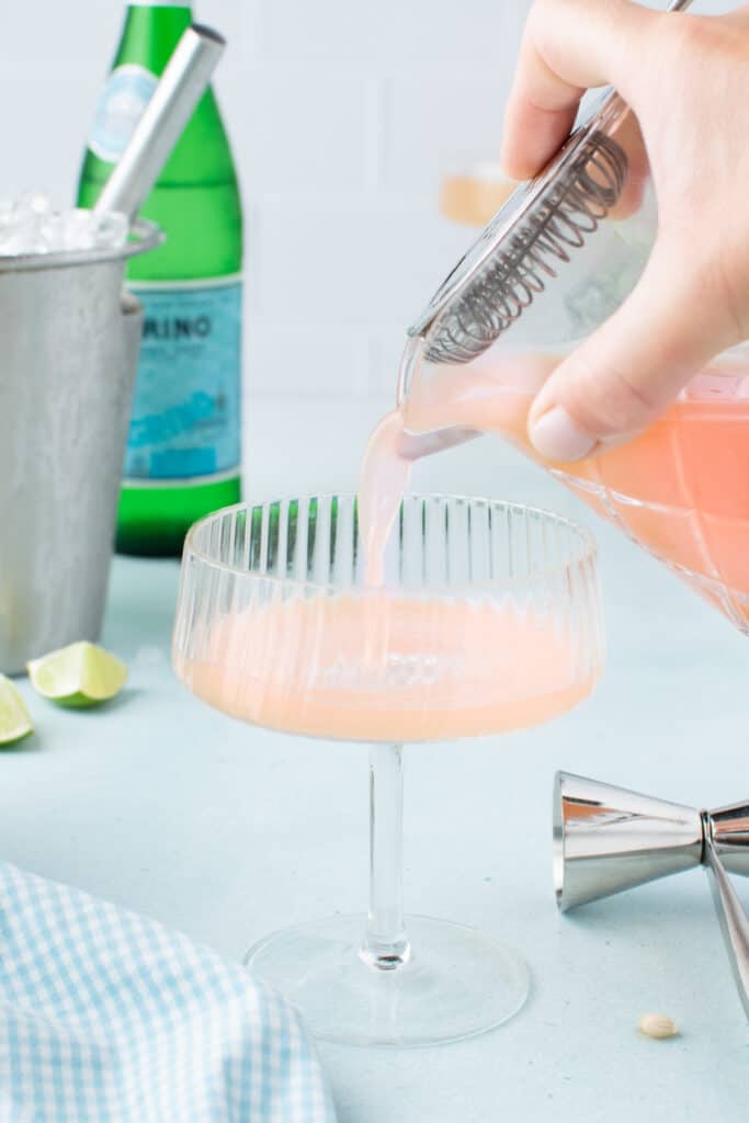 Straining a freshly mixed Paloma Cocktail into a coupe glass.