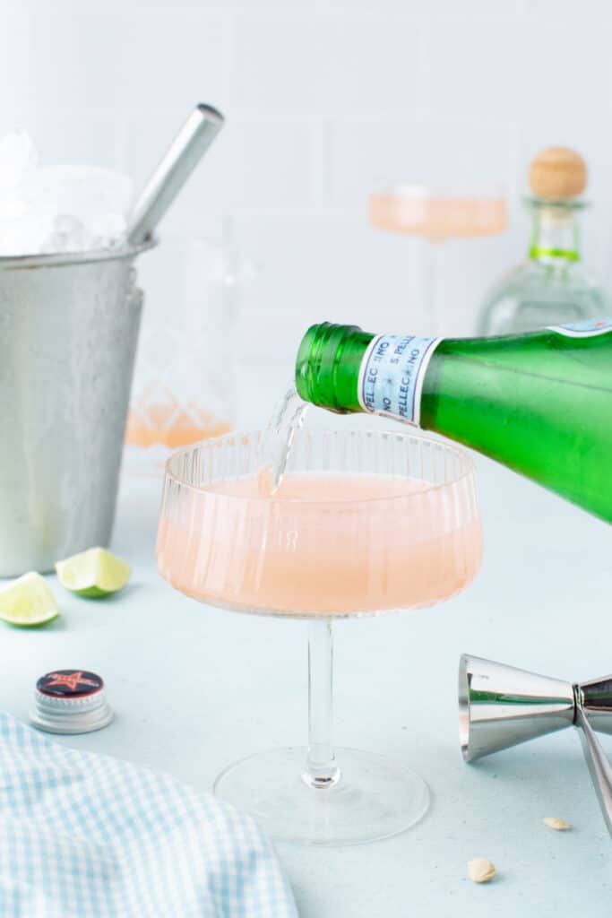 Topping a Paloma Cocktail with sparkling water before serving.