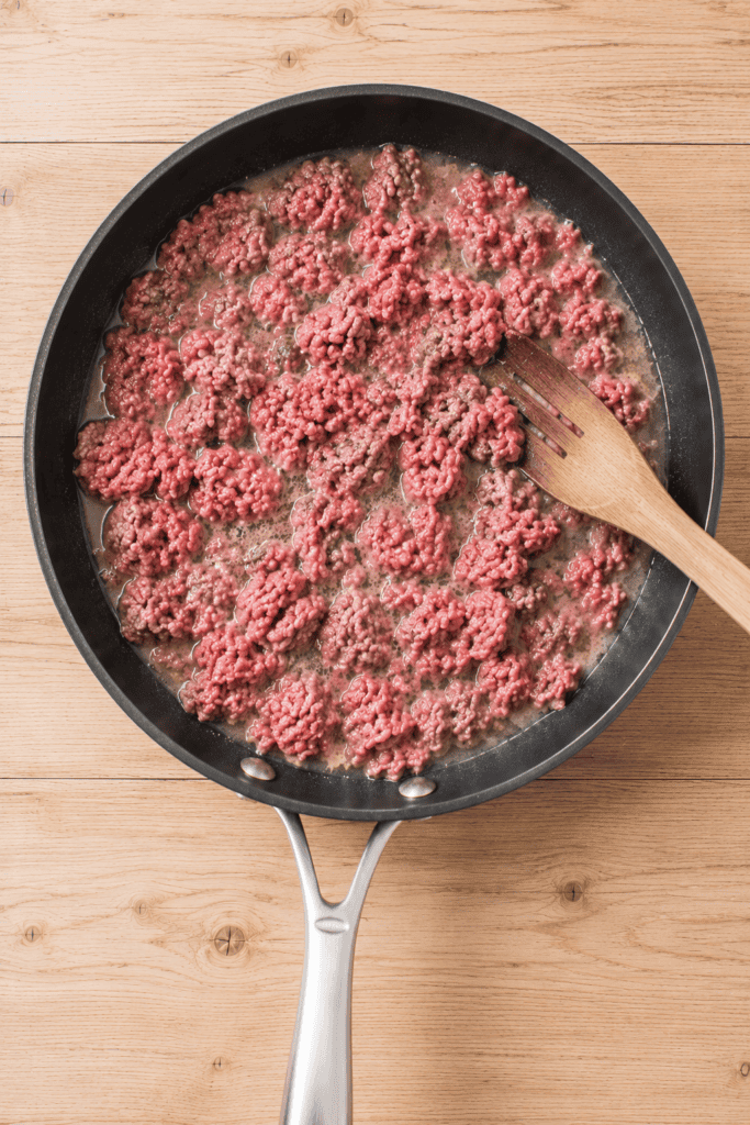 Ground beef cooking with water in a skillet for homemade hot dog chili.