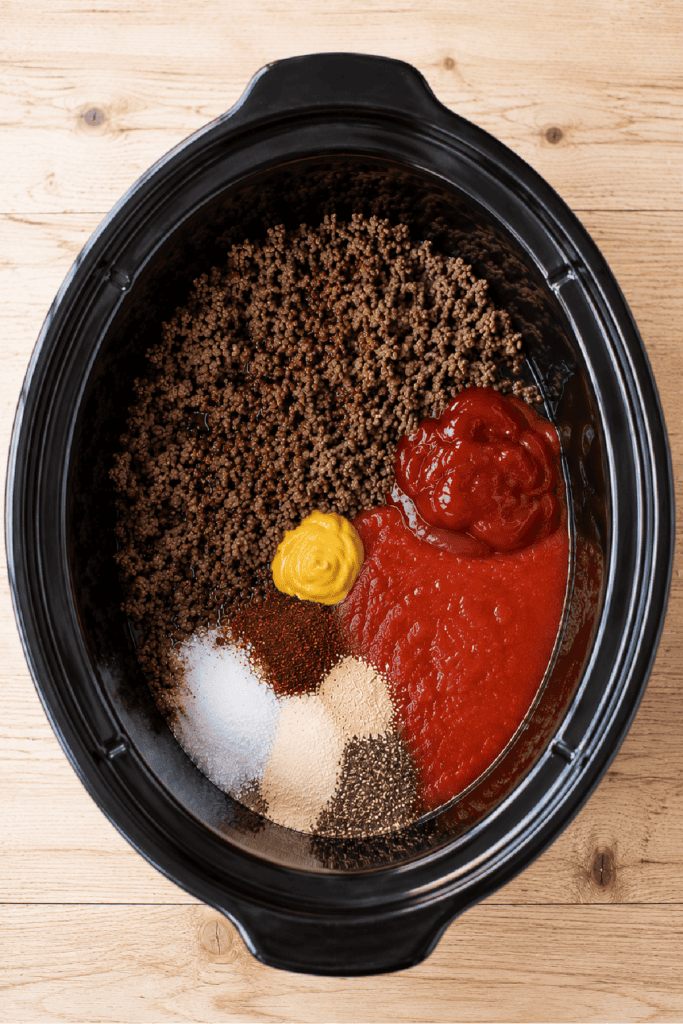 Ground beef and seasonings added to a slow cooker before cooking hot dog chili.