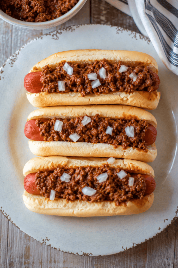Three homemade chili dogs topped with Slow Cooker Hot Dog Chili and diced onions.