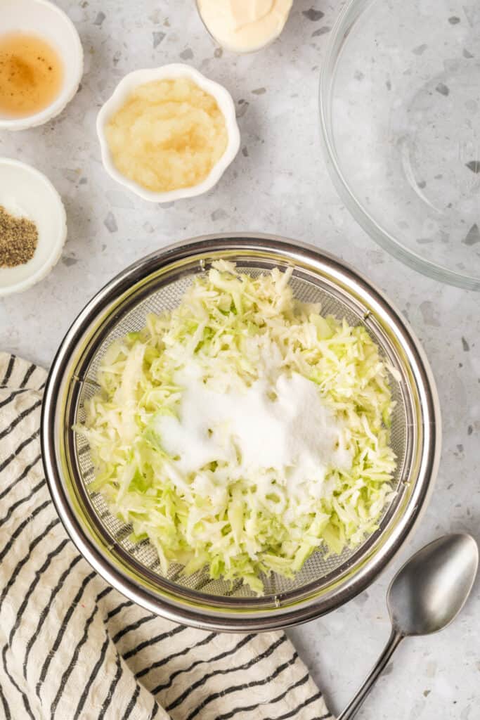 Shredded cabbage tossed with granulated sugar and salt in a colander before draining.