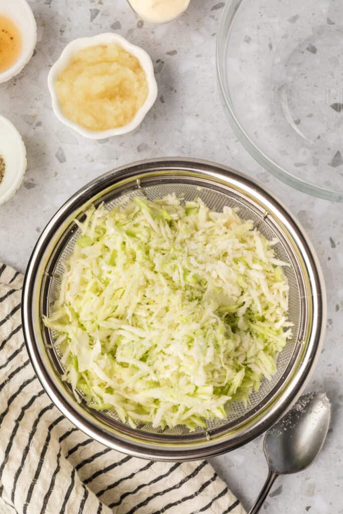 Close-up of shredded cabbage coated with sugar and salt before resting in a colander.