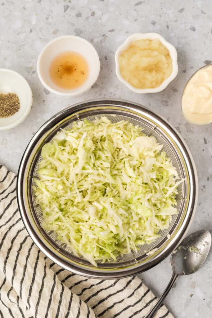 Shredded cabbage draining in a colander to remove excess moisture for homemade slaw.