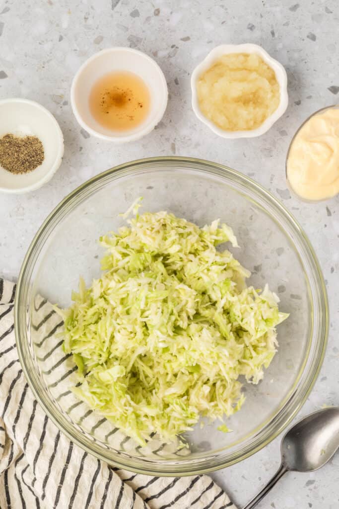 Drained shredded cabbage transferred to a glass mixing bowl before adding the dressing ingredients.
