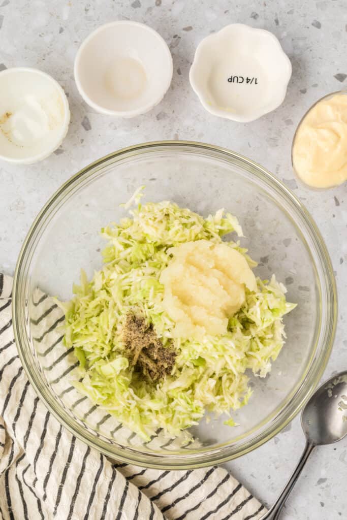 Shredded cabbage topped with grated onion, black pepper, and apple cider vinegar before mixing.