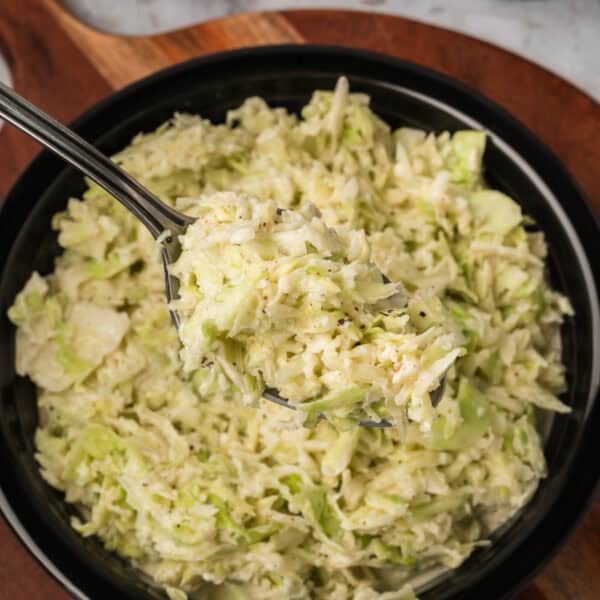 Southern-Style Slaw served in a black bowl with a spoonful of creamy homemade coleslaw lifted above the dish.
