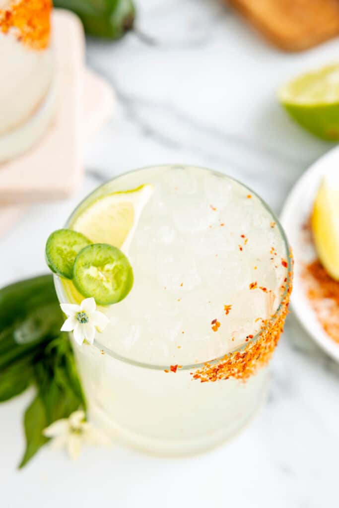 Spicy margarita recipe served over ice with fresh jalape&ntilde;o slices, a lime wedge, and a Taj&iacute;n rim