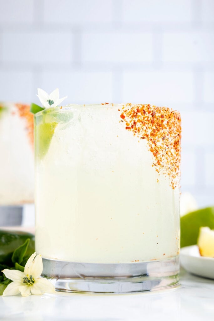 Close-up side view of a homemade jalapeño margarita with a Tajín rim and fresh lime garnish