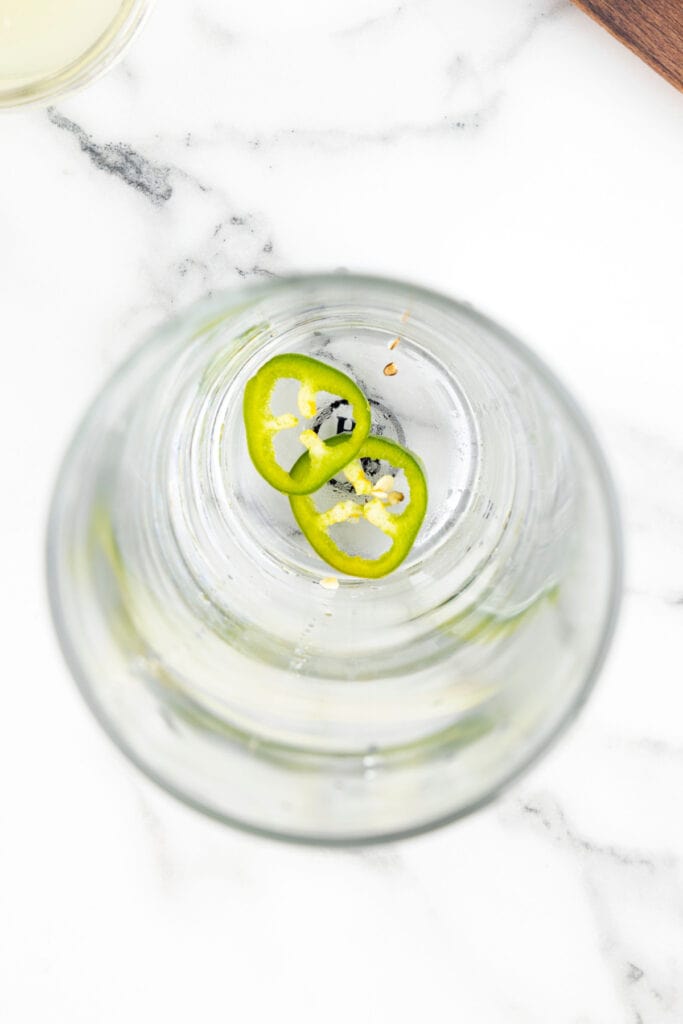 Fresh jalapeño slices in the bottom of a cocktail shaker before muddling