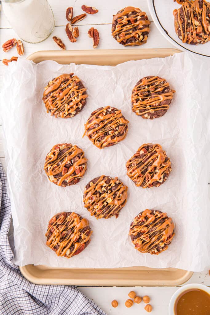 Freshly baked Easy Turtle Cookies with caramel drizzle cooling on a parchment-lined baking sheet.