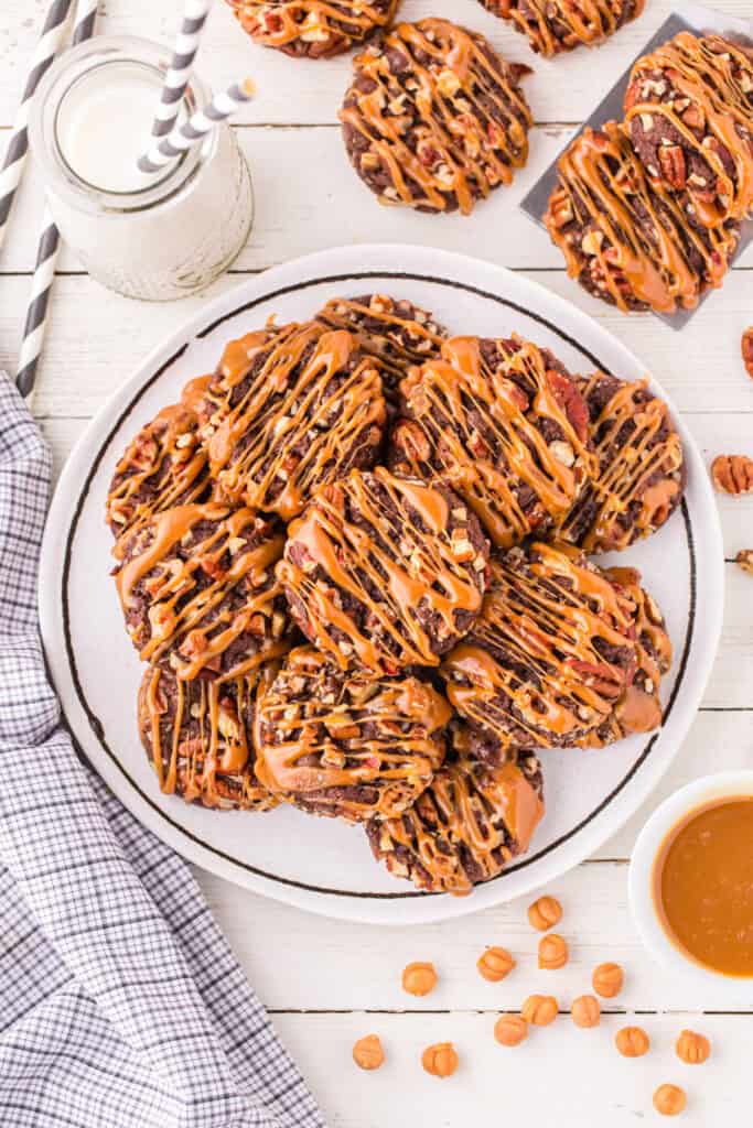 Platter filled with Easy Turtle Cookies drizzled with caramel and served with a glass of milk.