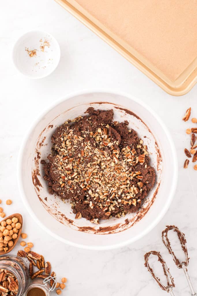 Chopped pecans being added to rich chocolate cookie dough for Easy Turtle Cookies.