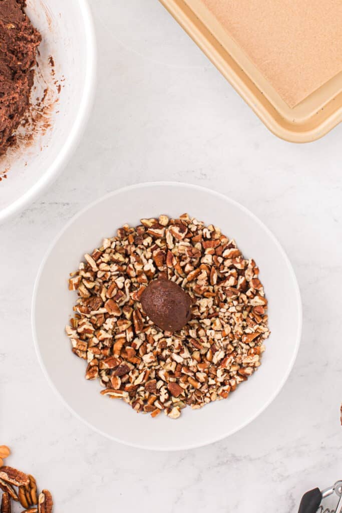 Ball of Easy Turtle Cookie dough rolled in chopped pecans before baking.