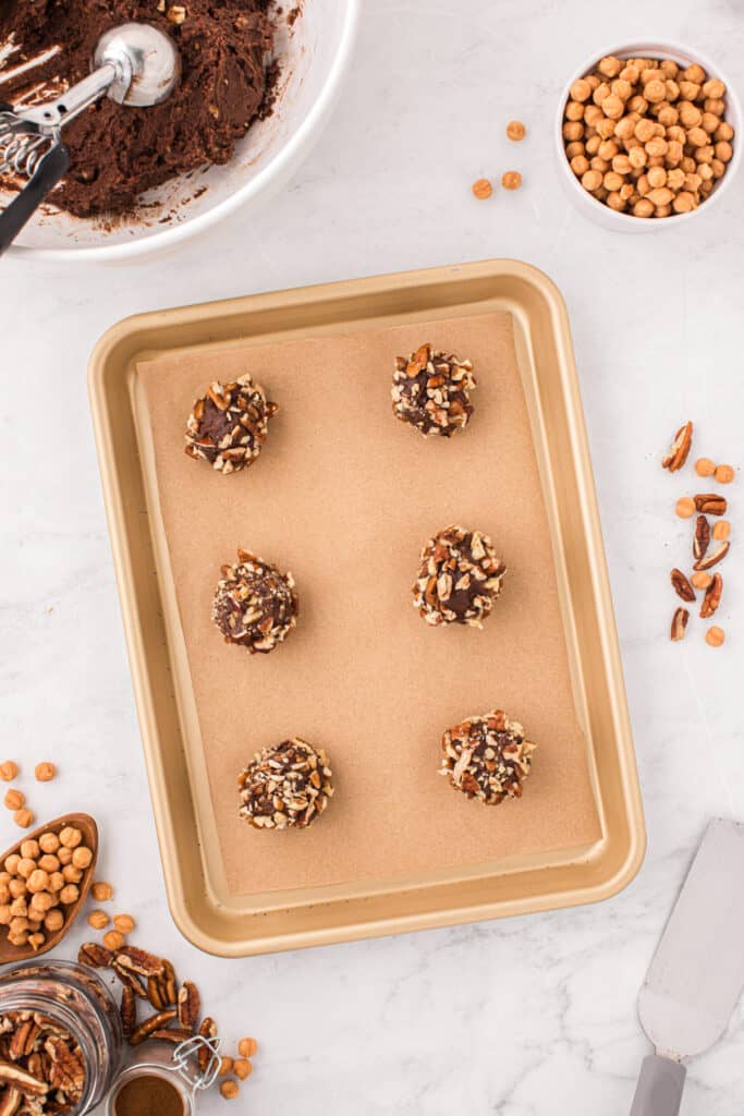Easy Turtle Cookie dough balls coated with pecans and arranged on a parchment-lined baking sheet before baking.