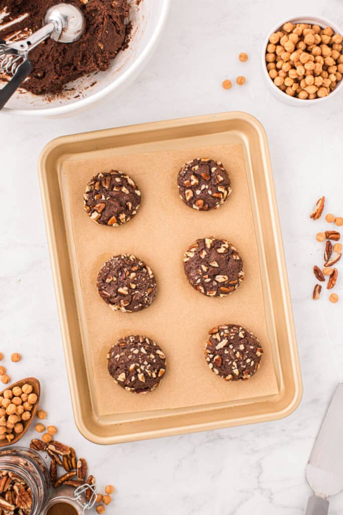 Baked Easy Turtle Cookies on a parchment-lined baking sheet before adding the caramel drizzle.