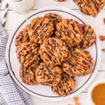 Square image of Easy Turtle Cookies piled on a serving plate with caramel drizzle and chopped pecans.