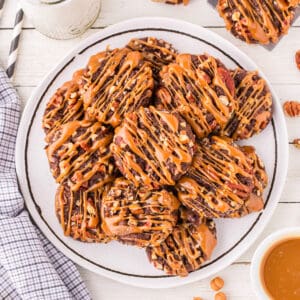 Square image of Easy Turtle Cookies piled on a serving plate with caramel drizzle and chopped pecans.
